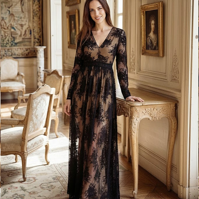Woman in a black lace dress standing in an elegant room with classical decor.