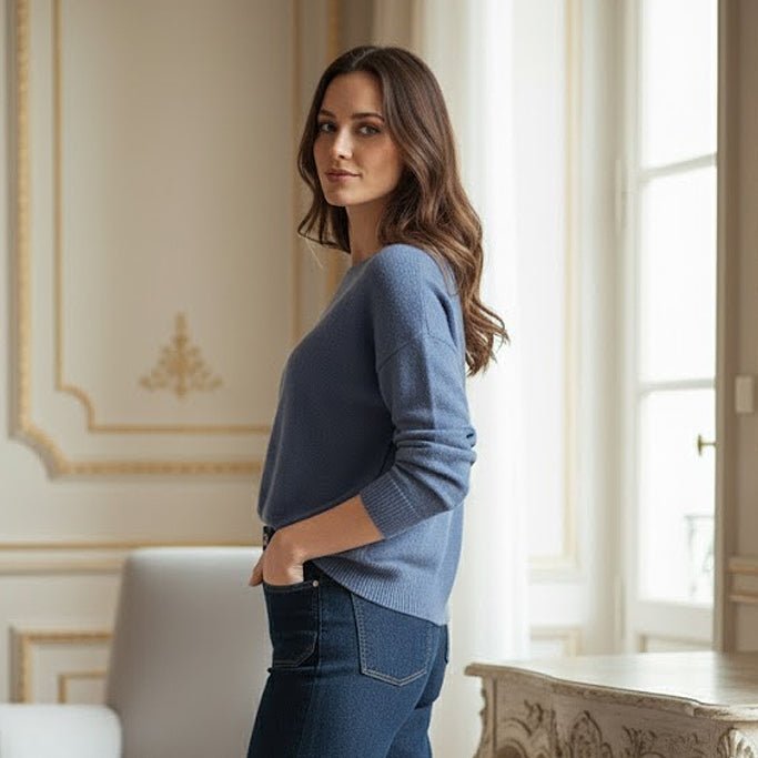 Woman wearing a blue sweater and jeans in an elegant room.